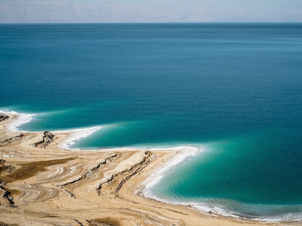 Aerial view of deep blue water meeting a light brown shoreline with white salt crusts along the Dead Sea.