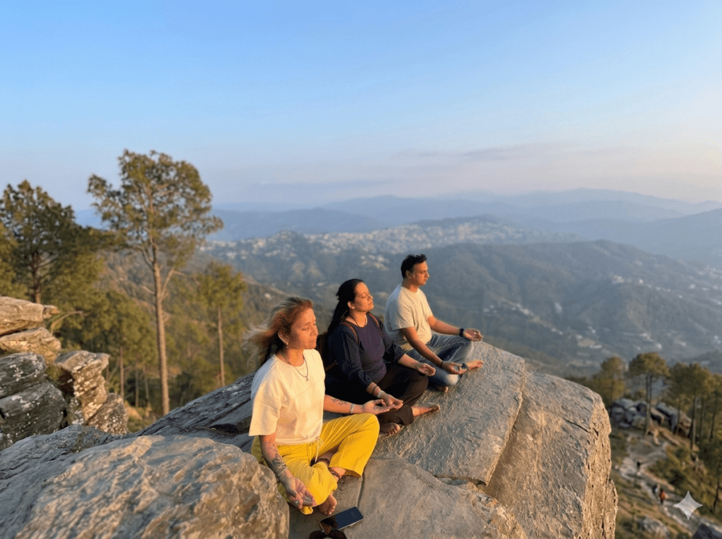 Three people meditating on a rock cliff overlooking the Himalayan hills near at sunset.