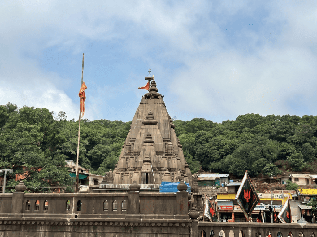 A stone temple spire with an orange flag, surrounded by green trees and a stone wall in the foreground