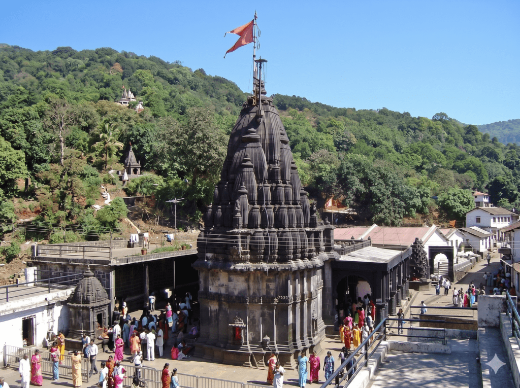 A high-angle view of the ancient, dark stone Bhimashankar Temple spire with an orange flag, surrounded by lush green hills and pilgrims