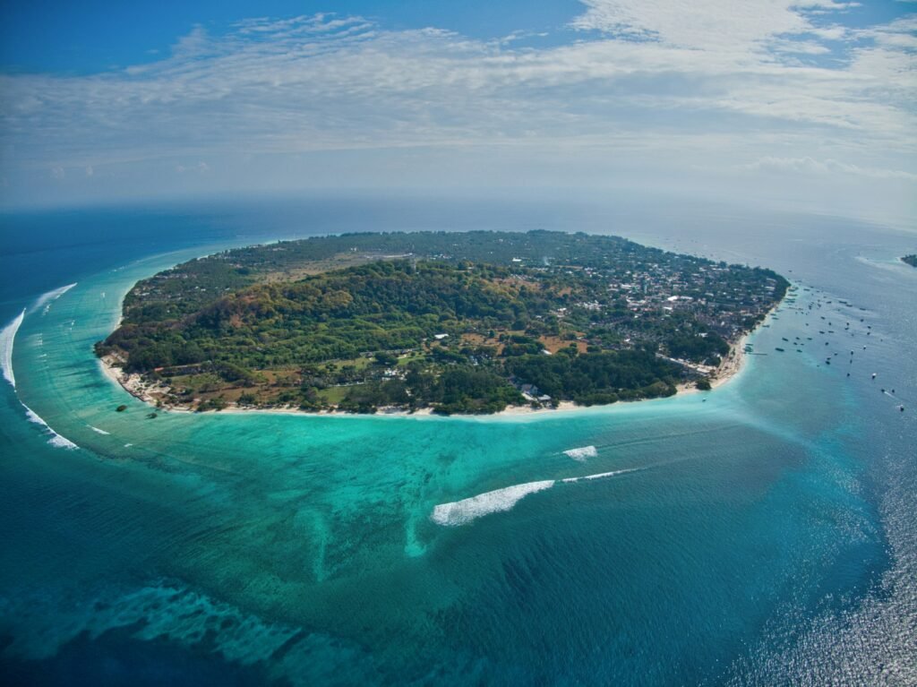 Aerial drone perspective of Gili Trawangan Island showing its lush green center and bright turquoise coastal waters.