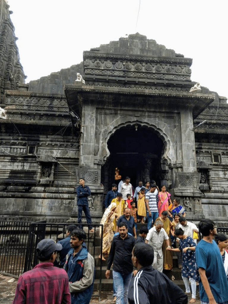 A crowded entrance of a grand, dark stone Hindu temple with intricate carvings and towering structures