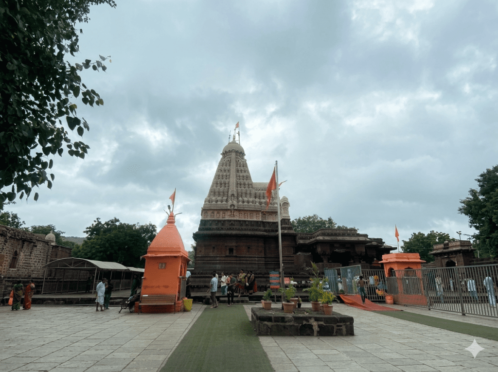 Traditional multi-layered spire of an ancient Indian temple courtyard with people walking around under a cloudy sky.