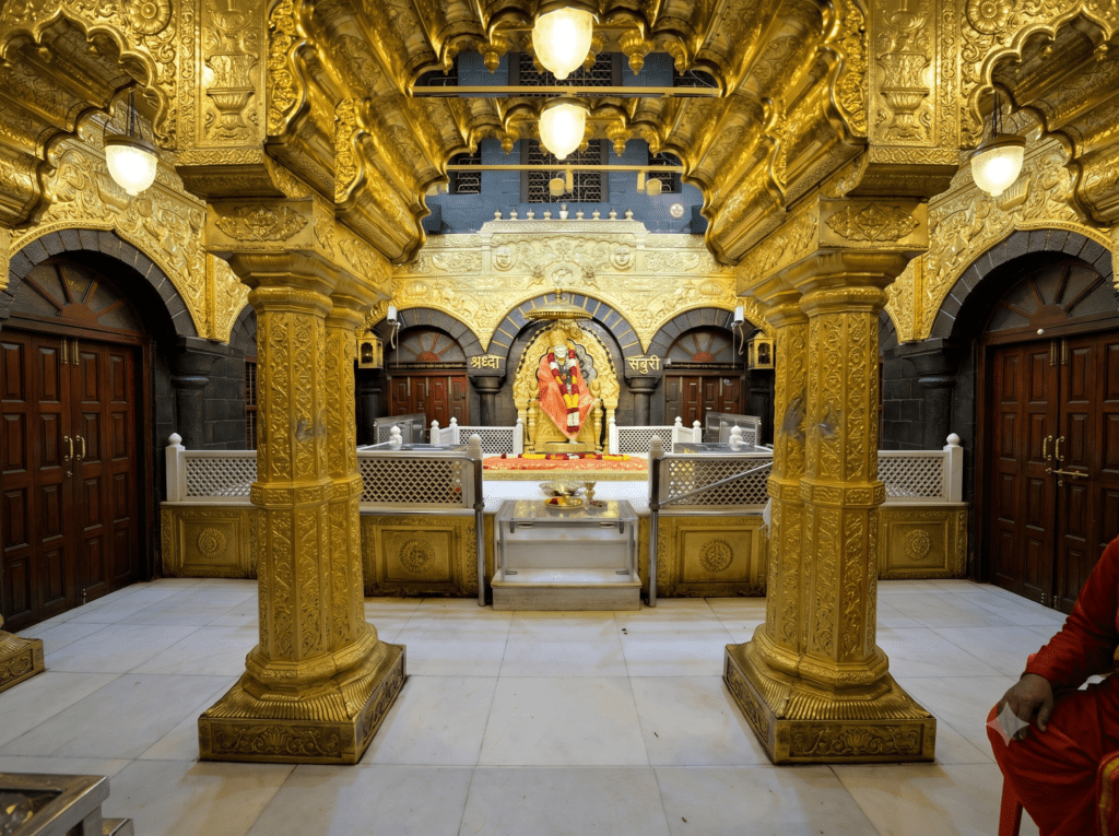 A golden temple interior showcasing the marble idol of Shirdi Sai Baba seated under an ornate golden canopy.