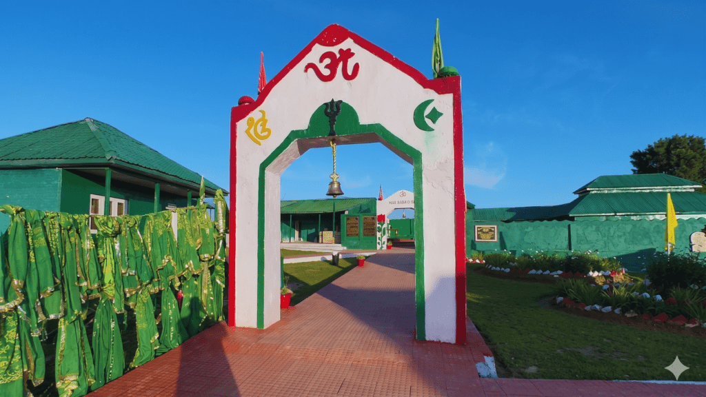 A white and red archway adorned with religious symbols and a hanging bell marks the pathway to a green-painted shrine complex.