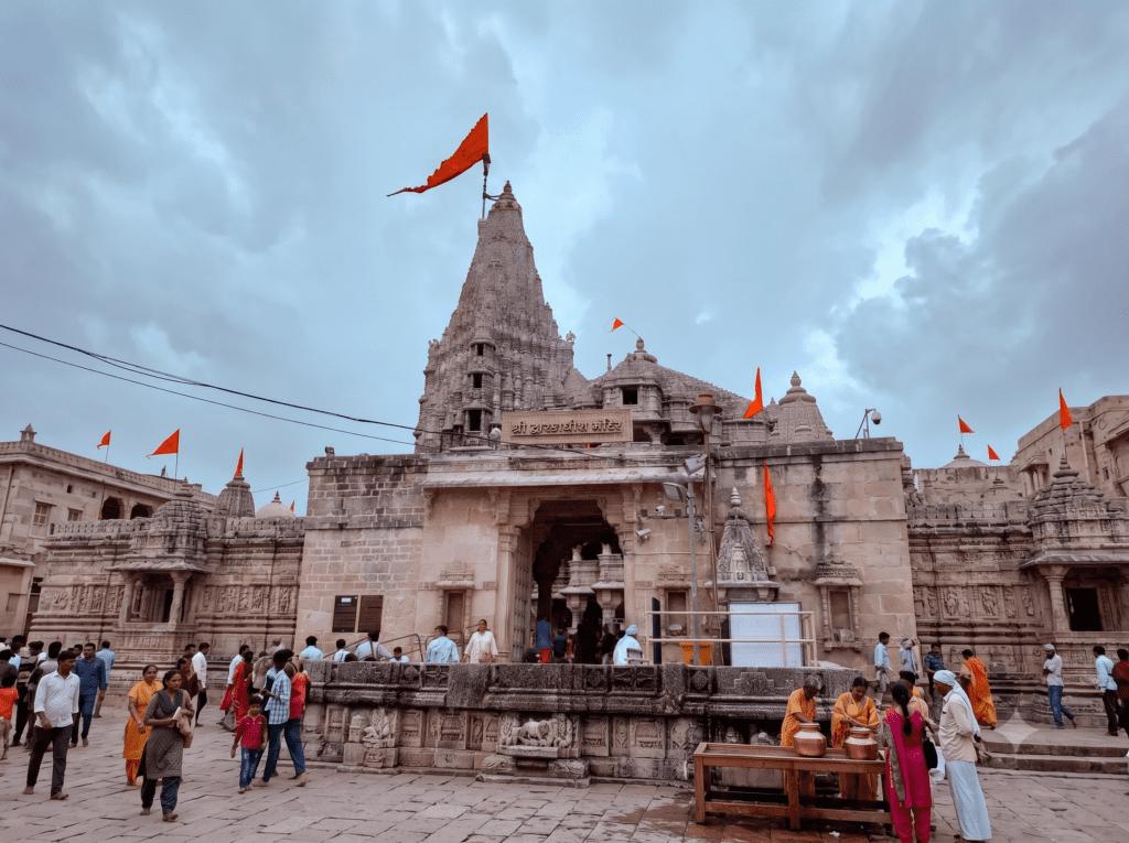 Front view of the ancient stone Dwarkadhish Temple with a large orange flag waving from its tall carved spire under a cloudy sky.