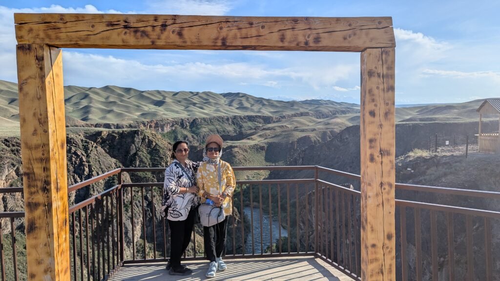 Two women standing at a black canyon overlook framed by large wooden beams.