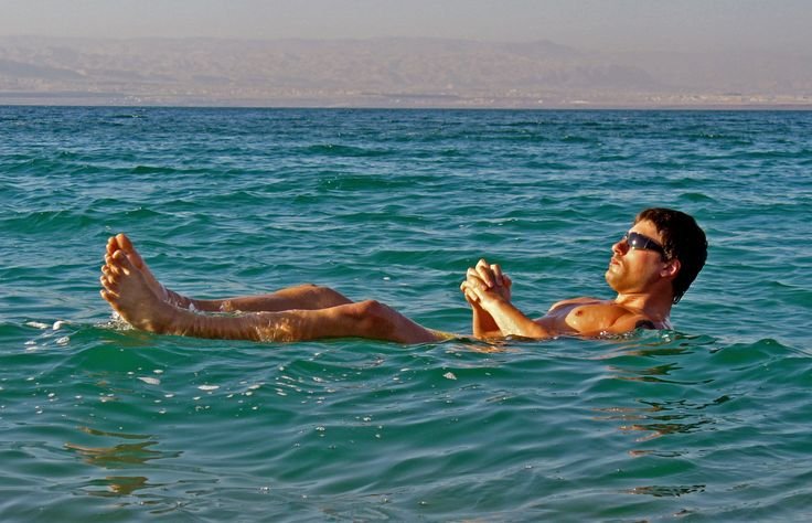 A man wearing sunglasses floating relaxed on his back in deep blue-green Dead Sea water.