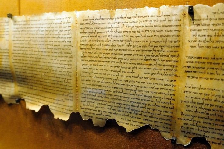 An unrolled ancient parchment manuscript displaying Hebrew text with frayed, weathered edges.