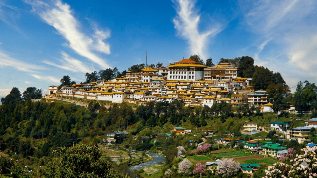 A vibrant artistic landscape of the Tawang Monastery in Arunachal Pradesh during spring, showcasing the multi-tiered complex with golden and red roofs nestled among forests in full bloom with pink and white flowers under a clear blue sky with stylized clouds.
