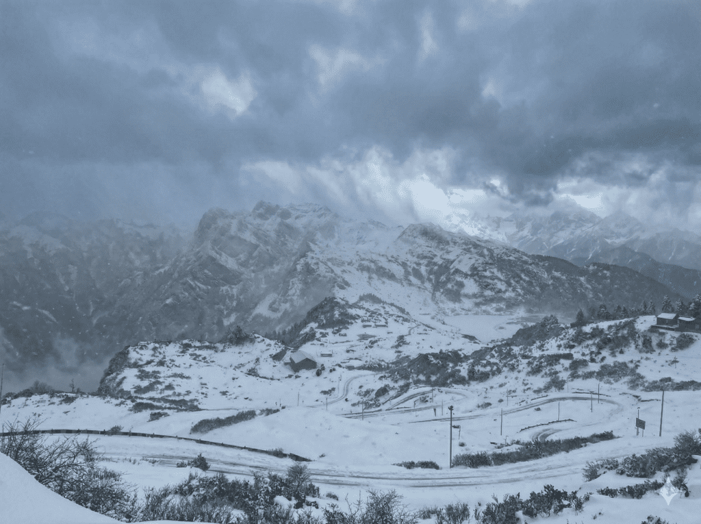 A bleak, snow-covered mountain landscape at Bum La Pass under a stormy, grey sky with heavy clouds and mist.
