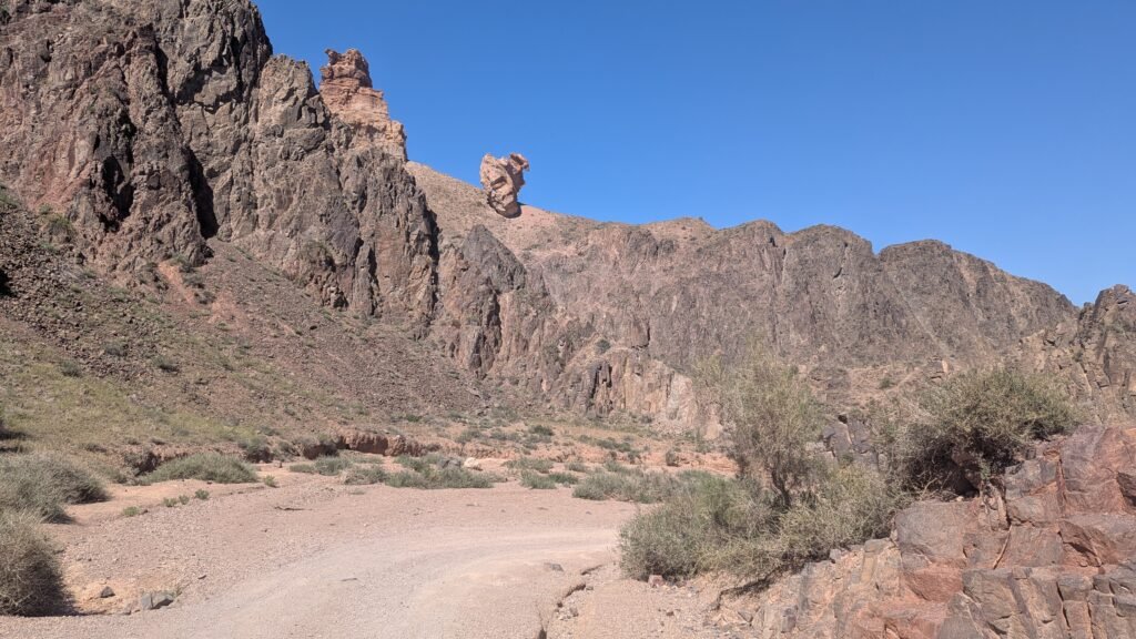 Rocky desert canyon under a clear blue sky with a dirt road leading through the landscape.