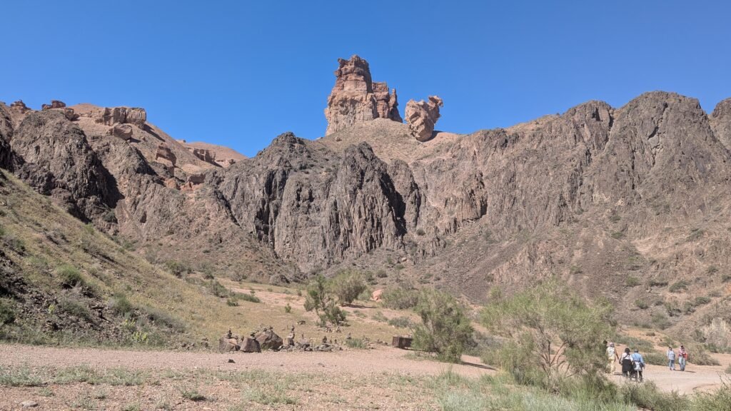 Panoramic view featuring rugged brown rock towers and mountains under a clear blue sky.